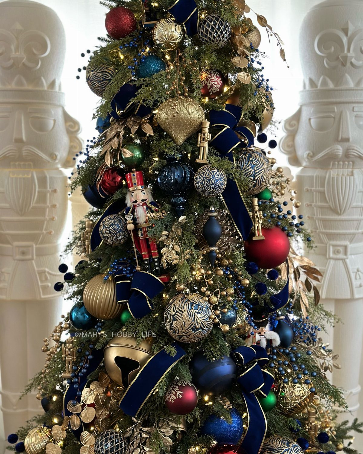 A Christmas tree decorated with blue and gold ornaments, navy velvet ribbons, and small nutcracker figurines.