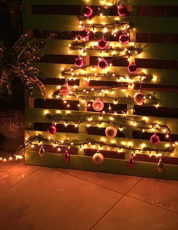 A green wooden pallet decorated with fairy lights and ornaments in a tree shape.