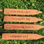 Terracotta herb garden signs with puns lying on green grass.