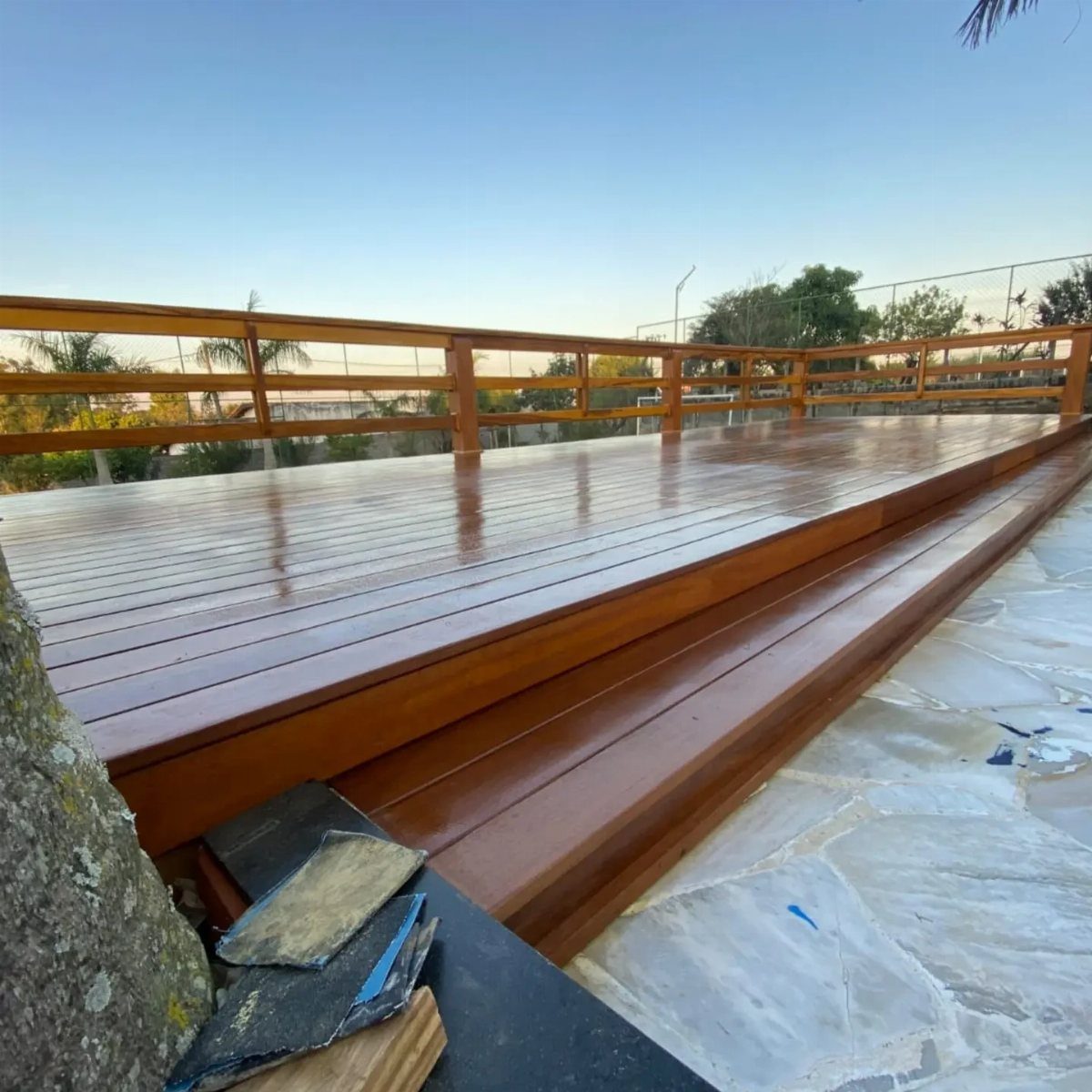 A polished reddish-brown wooden deck with steps and a railing on a stone patio.
