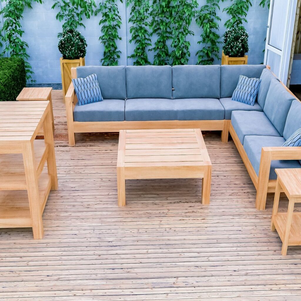 Light wood outdoor sectional sofa with blue cushions on a wooden deck with a coffee table.