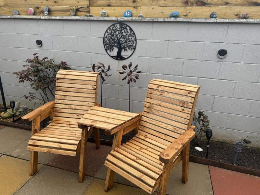 Two wooden lounge chairs and a small wooden side table on a patio.