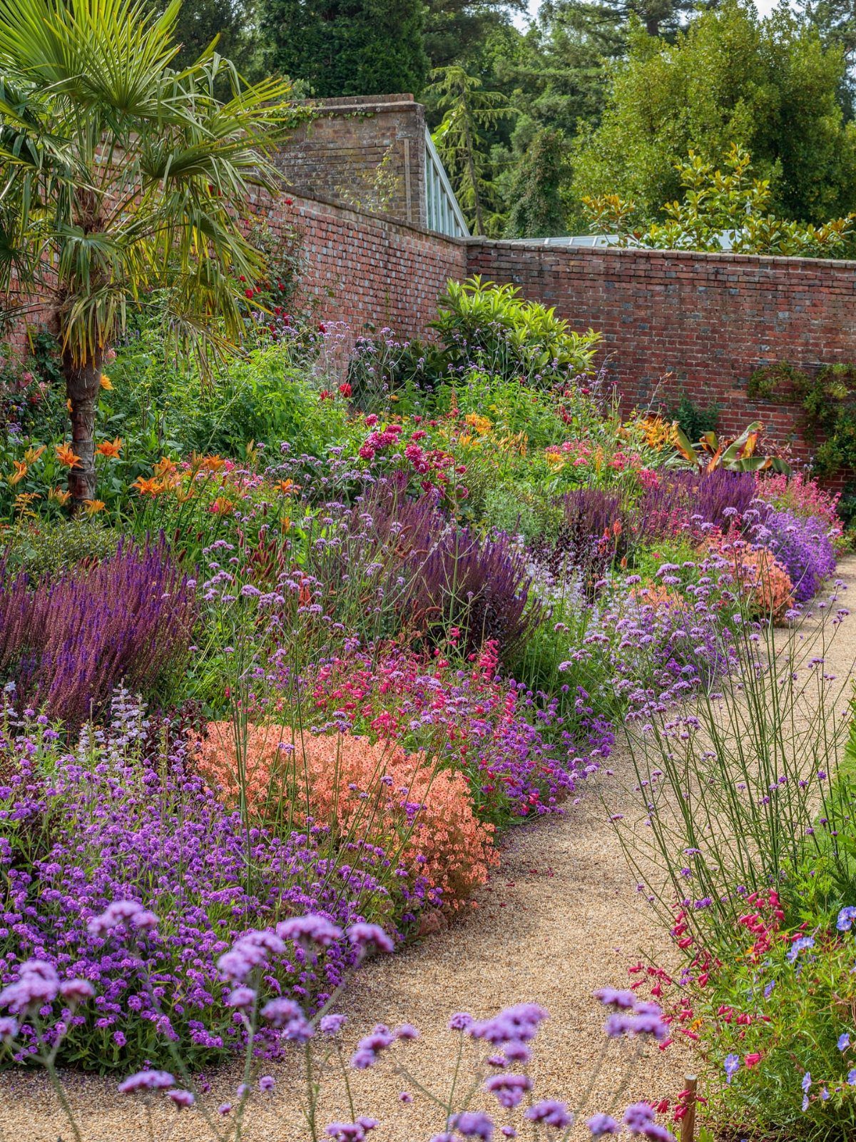 Colorful flowers in various shades of purple and pink growing along a gravel garden path.