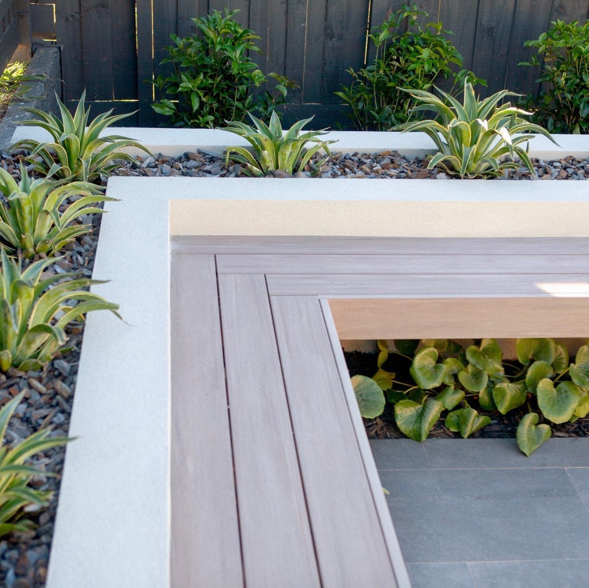 Built-in wooden bench seating integrated into a modern concrete garden structure with green plants.