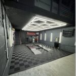 Black and grey checkered interlocking garage tiles covering a modern workshop floor with car lift.