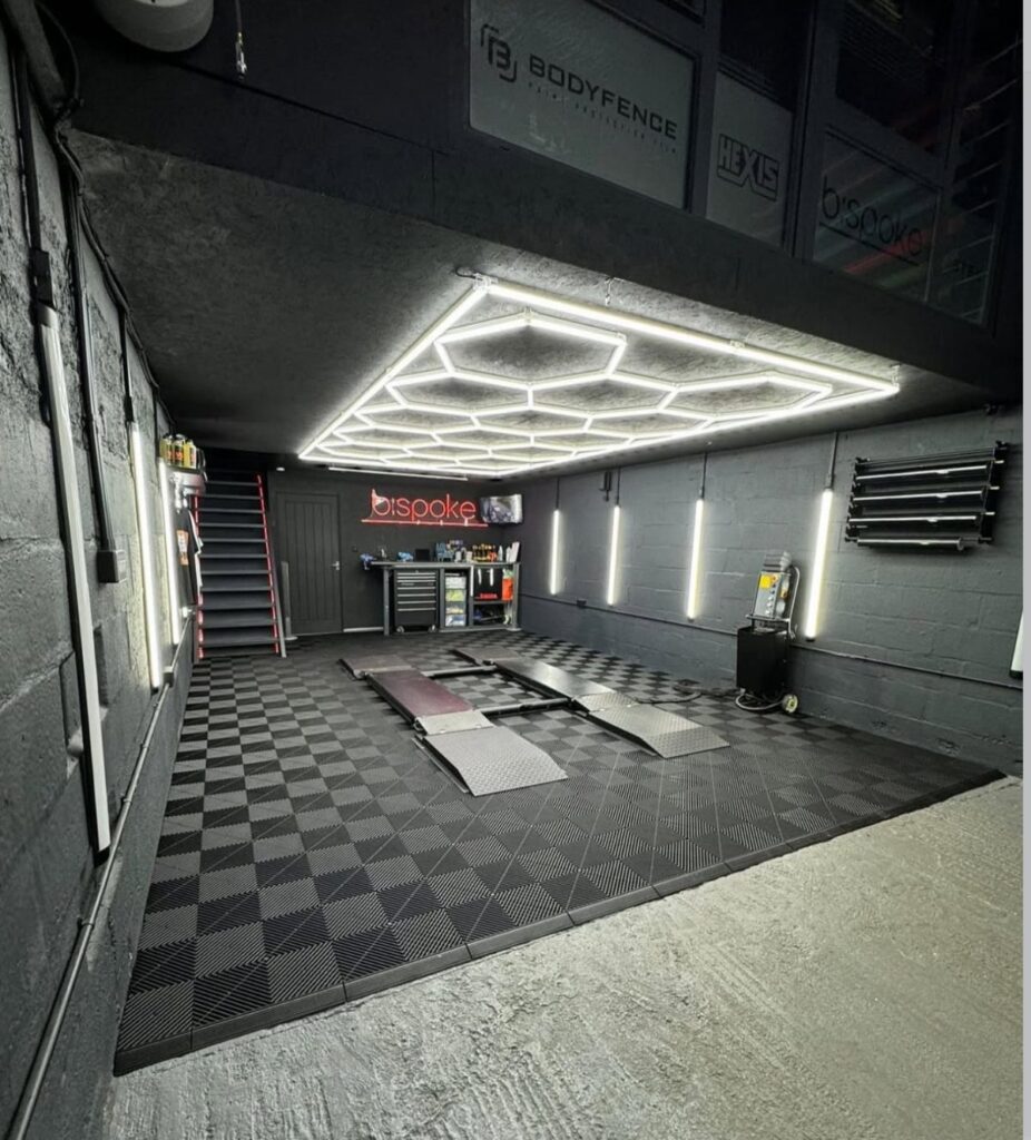 Black and grey checkered interlocking garage tiles covering a modern workshop floor with car lift.