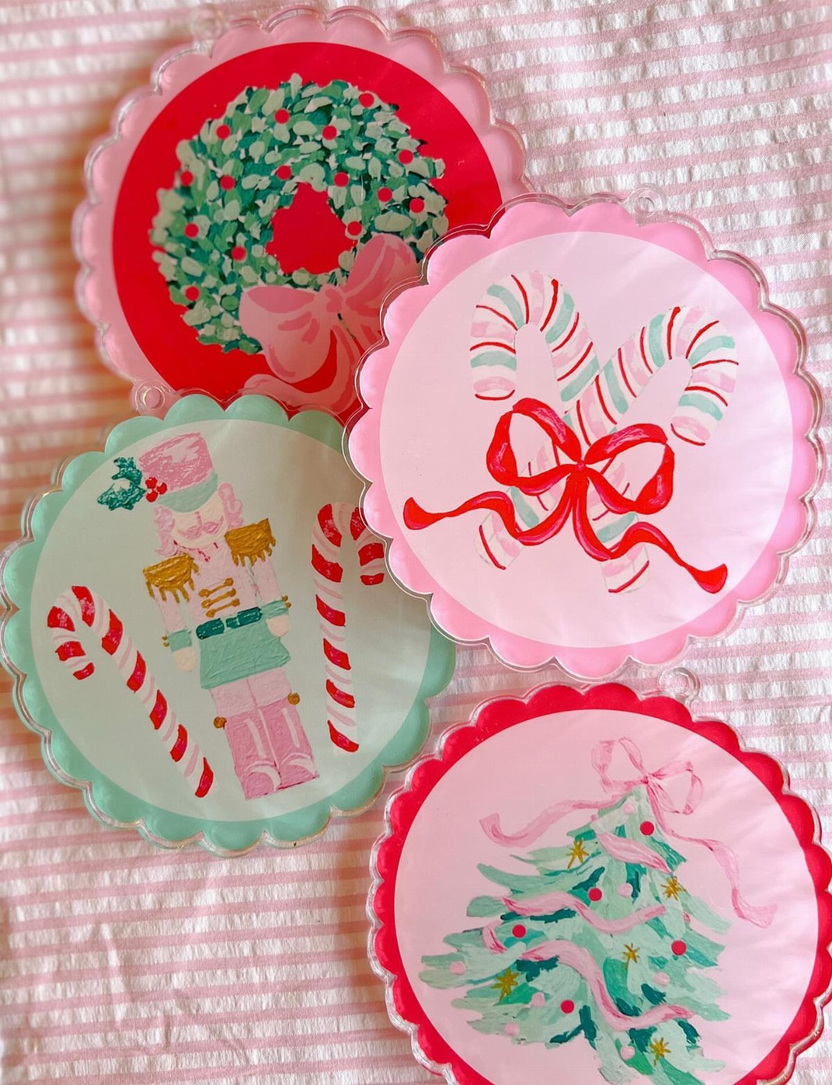 Four scalloped circular ornaments featuring hand-painted pastel holiday designs like a wreath, nutcracker, and Christmas tree.